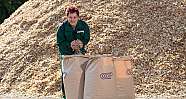 Frau hält Holzspäne vor großen Säcken und einem großen Holzspänehaufen