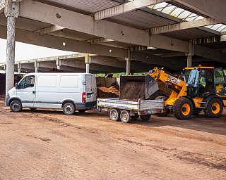 Ein Bagger lädt Erde in einen Anhänger hinter einem Transporter.