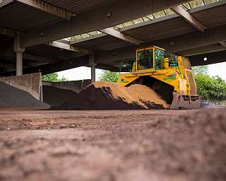 Eine gelbe Maschine bewegt verschiedene Materialien in einer Lagerhalle.
