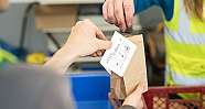 Zwei Personen tauschen einen kleinen Erdklumpen und eine Papierkarte in einer braunen Tüte