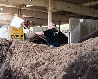 Mann schaufelt Material mit großem Metallwerkzeug in Halle mit Betonstützen