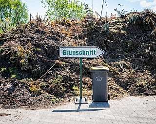 Richtiges Sammeln von Grünschnitt mit Schild und Mülltonne vor Komposthaufen