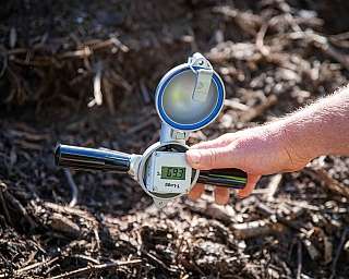 Person hält digitales Bodenthermometer über Erde zur Temperaturmessung