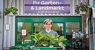 Frau vor Gartencenter hält Tablett mit mehreren grünen Topfpflanzen